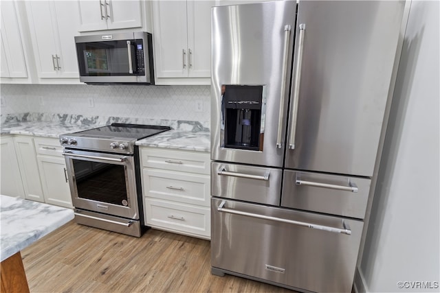 kitchen with appliances with stainless steel finishes, light hardwood / wood-style floors, white cabinetry, and tasteful backsplash