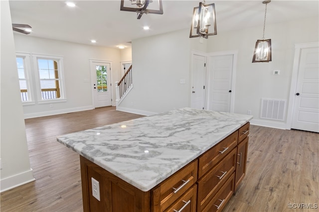 kitchen with wood-type flooring, pendant lighting, light stone counters, and a kitchen island