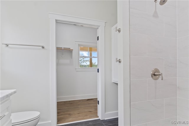 bathroom featuring a tile shower, vanity, hardwood / wood-style floors, and toilet