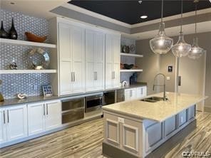 kitchen featuring tasteful backsplash, white cabinets, a center island with sink, pendant lighting, and sink