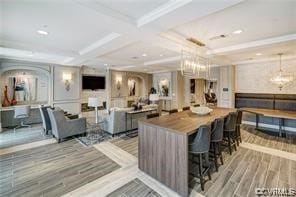 kitchen with coffered ceiling, beamed ceiling, a kitchen bar, light wood-type flooring, and pendant lighting