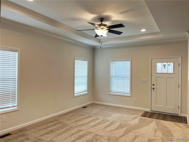 carpeted foyer entrance featuring visible vents, a ceiling fan, baseboards, crown molding, and a raised ceiling