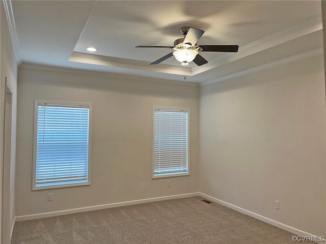 empty room with a ceiling fan, carpet, baseboards, ornamental molding, and a raised ceiling