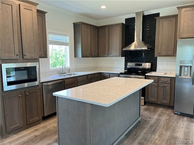 kitchen with a sink, wall chimney range hood, light wood-style flooring, and stainless steel appliances