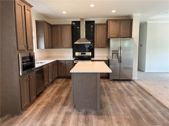 kitchen featuring crown molding, wall chimney range hood, appliances with stainless steel finishes, and a center island