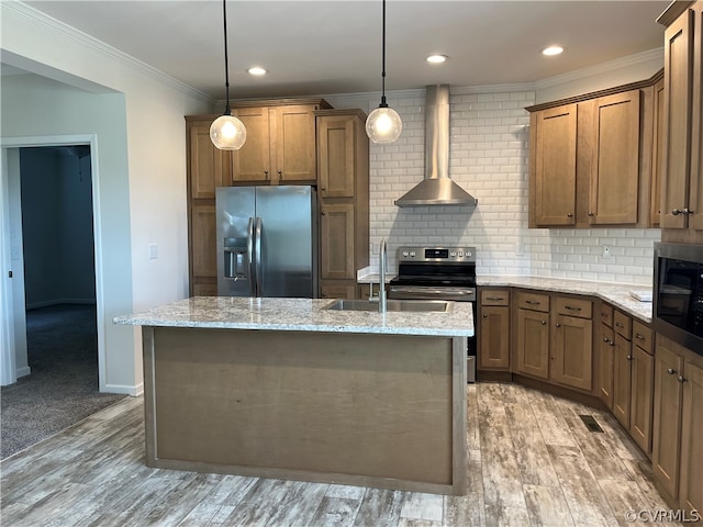 kitchen with appliances with stainless steel finishes, wall chimney exhaust hood, a kitchen island with sink, light carpet, and hanging light fixtures