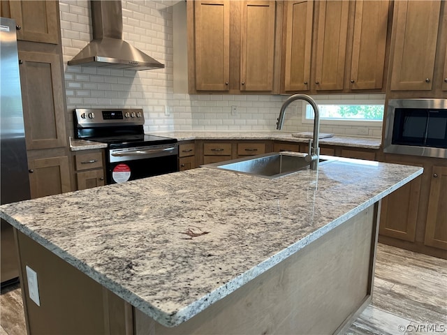 kitchen with a sink, tasteful backsplash, light wood-style floors, appliances with stainless steel finishes, and wall chimney exhaust hood