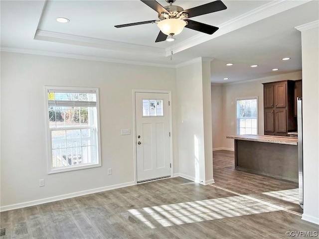 entryway with ornamental molding, a tray ceiling, and wood finished floors