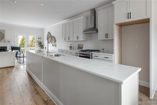 kitchen with light hardwood / wood-style floors, french doors, gas range, wall chimney exhaust hood, and a kitchen island with sink