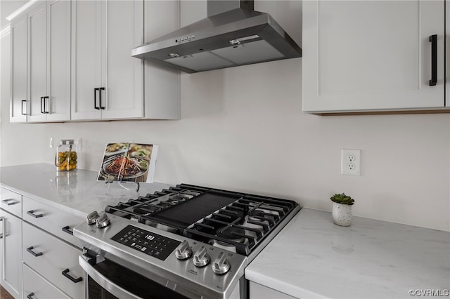 kitchen featuring wall chimney range hood, stainless steel gas stove, white cabinetry, and light stone countertops