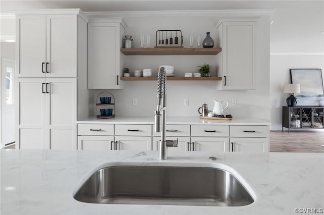 kitchen featuring white cabinets, light stone countertops, wood-type flooring, and sink