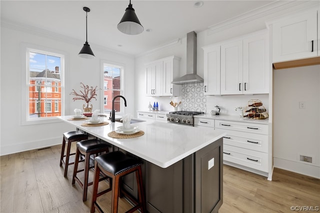 kitchen featuring hanging light fixtures, light wood-type flooring, wall chimney range hood, an island with sink, and sink