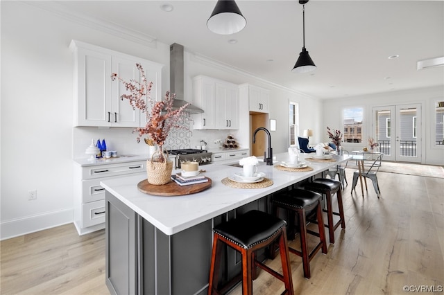 kitchen featuring a kitchen island with sink, a kitchen bar, light hardwood / wood-style floors, white cabinets, and wall chimney range hood