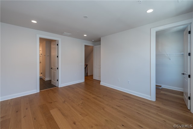 unfurnished bedroom featuring a closet, ensuite bath, wood-type flooring, and a spacious closet