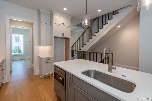 kitchen featuring stainless steel microwave, light wood-type flooring, hanging light fixtures, decorative backsplash, and sink