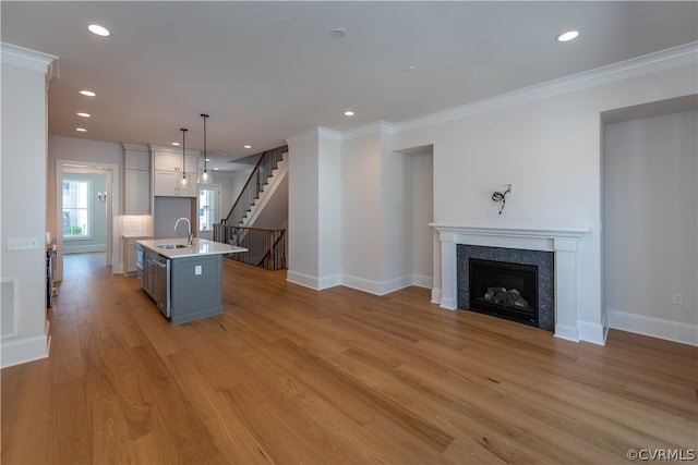 kitchen with white cabinetry, hanging light fixtures, sink, a center island with sink, and light hardwood / wood-style floors