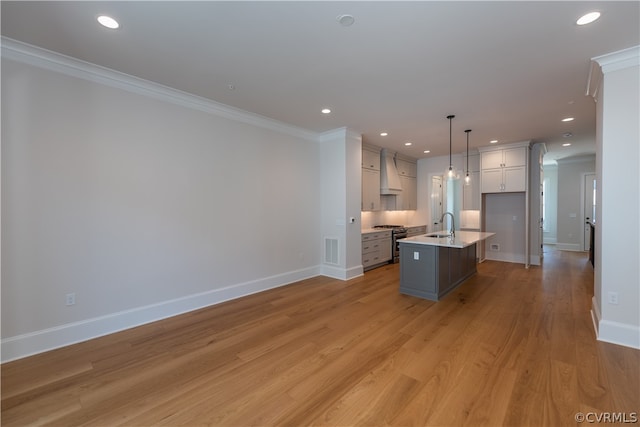 kitchen featuring gas stove, light hardwood / wood-style floors, custom exhaust hood, decorative light fixtures, and a center island with sink