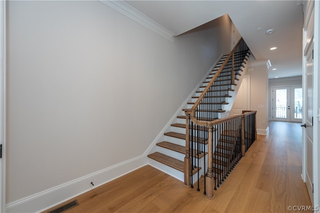 staircase with ornamental molding, french doors, and light hardwood / wood-style floors