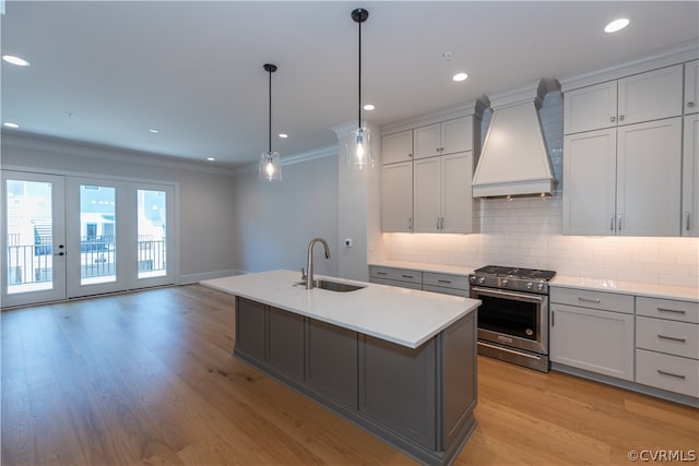 kitchen featuring stainless steel range with gas stovetop, premium range hood, decorative backsplash, ornamental molding, and light hardwood / wood-style floors