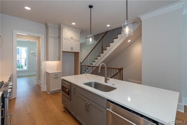 kitchen featuring appliances with stainless steel finishes, light hardwood / wood-style flooring, sink, hanging light fixtures, and ornamental molding