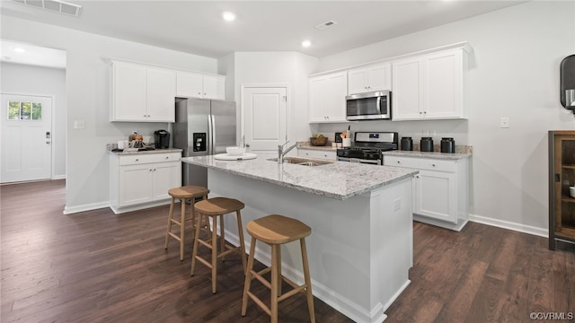 kitchen with light stone countertops, an island with sink, dark wood-type flooring, stainless steel appliances, and white cabinetry