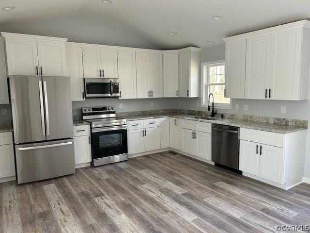 kitchen with sink, vaulted ceiling, white cabinets, and appliances with stainless steel finishes