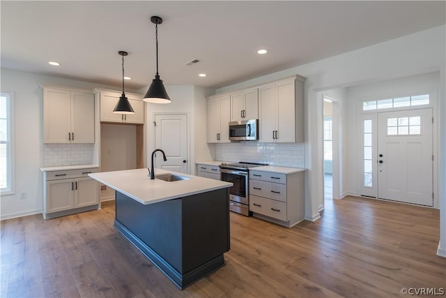 kitchen featuring pendant lighting, a center island with sink, sink, light hardwood / wood-style flooring, and appliances with stainless steel finishes