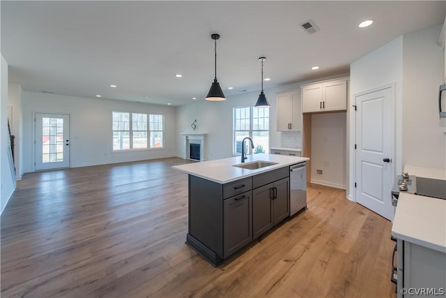 kitchen with sink, hanging light fixtures, stainless steel dishwasher, light wood-type flooring, and an island with sink