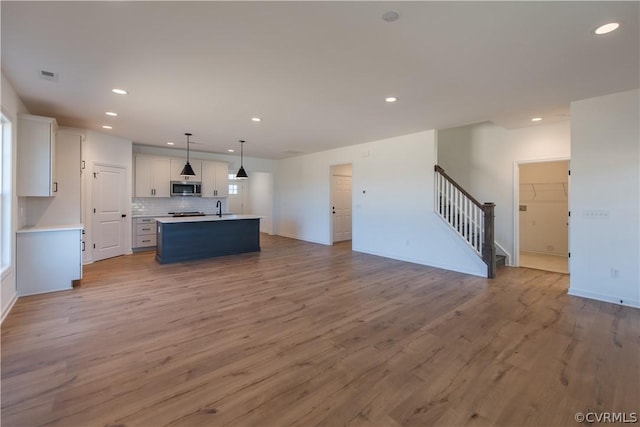 kitchen with an island with sink, tasteful backsplash, decorative light fixtures, light hardwood / wood-style floors, and white cabinetry