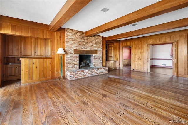 unfurnished living room featuring beamed ceiling, a fireplace, and wood walls