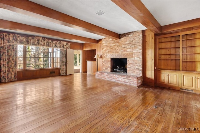 unfurnished living room with wooden walls, a fireplace, hardwood / wood-style floors, and beam ceiling