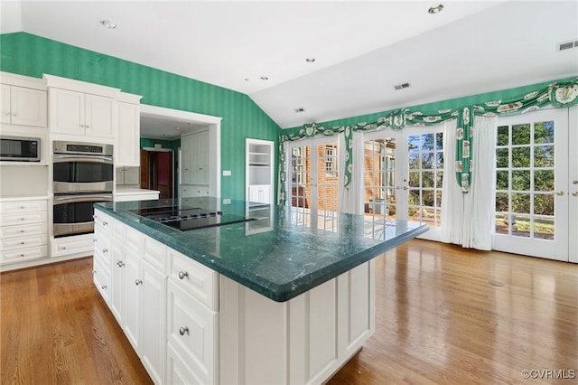 kitchen with appliances with stainless steel finishes, lofted ceiling, white cabinets, a center island, and french doors