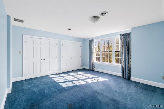 unfurnished bedroom featuring two closets and dark colored carpet