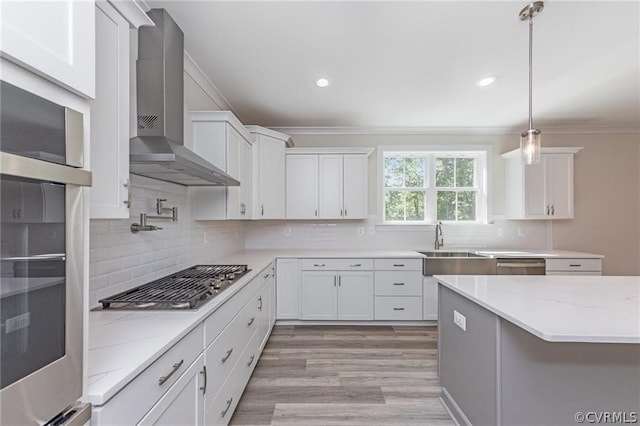 kitchen featuring white cabinetry, wall chimney range hood, light hardwood / wood-style floors, pendant lighting, and tasteful backsplash