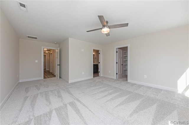 unfurnished bedroom with ceiling fan, a walk in closet, connected bathroom, and light carpet