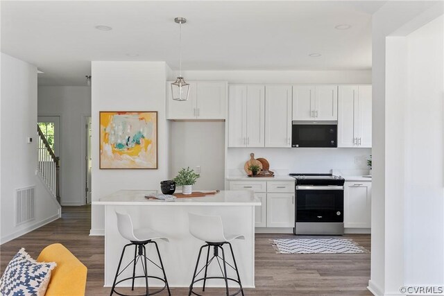 kitchen with a kitchen bar, decorative light fixtures, electric stove, white cabinets, and a center island