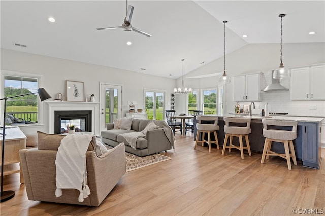 living room featuring a wealth of natural light, light hardwood / wood-style flooring, ceiling fan with notable chandelier, and sink