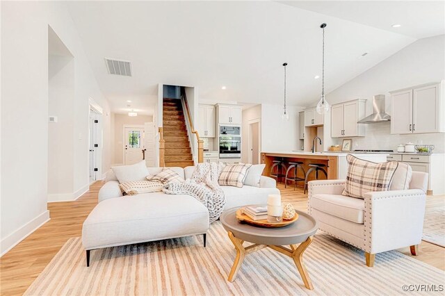 living area featuring light wood-type flooring, stairs, lofted ceiling, baseboards, and recessed lighting