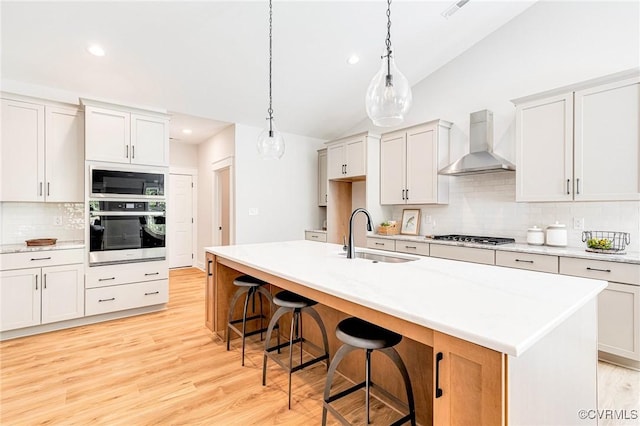 kitchen featuring stainless steel appliances, wall chimney range hood, a sink, vaulted ceiling, and decorative backsplash