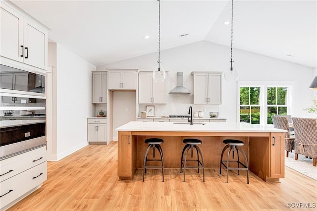 kitchen featuring stainless steel oven, wall chimney range hood, a sink, built in microwave, and light countertops