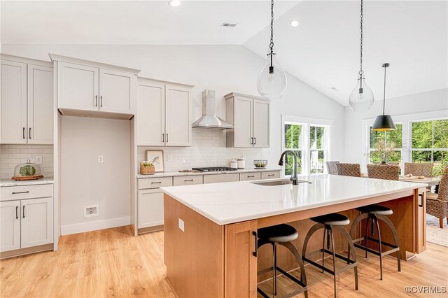 kitchen featuring a sink, wall chimney range hood, vaulted ceiling, light wood-style floors, and backsplash