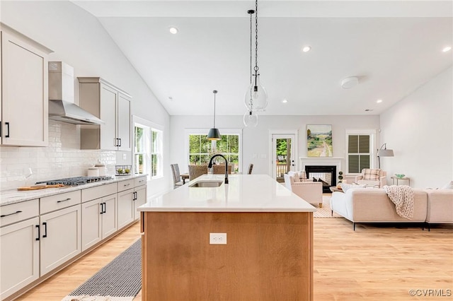 kitchen with a sink, wall chimney exhaust hood, light wood-style floors, stainless steel gas stovetop, and decorative backsplash