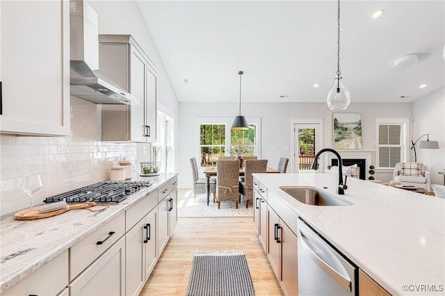 kitchen featuring a sink, wall chimney exhaust hood, appliances with stainless steel finishes, light wood-style floors, and decorative backsplash