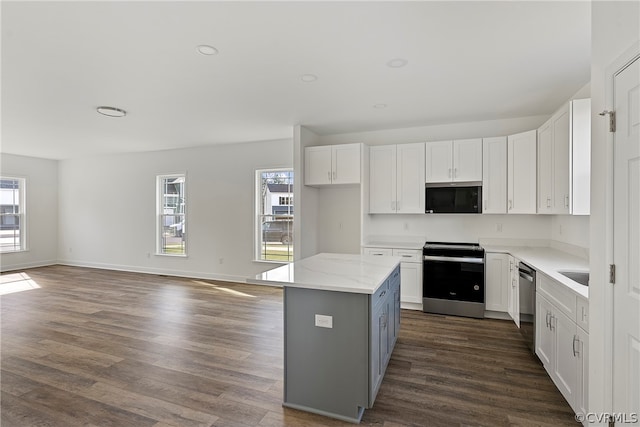 kitchen with stainless steel appliances, a center island, light stone countertops, dark wood-type flooring, and white cabinetry