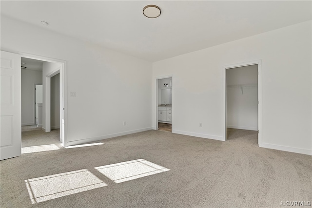 unfurnished bedroom with a closet, ensuite bath, a spacious closet, and light colored carpet