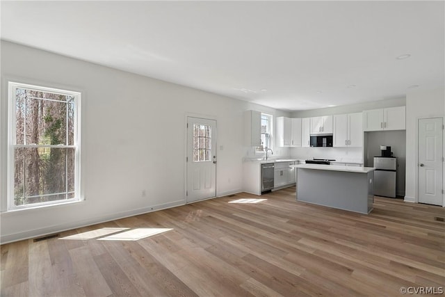 kitchen with light wood-style flooring, a kitchen island, appliances with stainless steel finishes, white cabinets, and light countertops