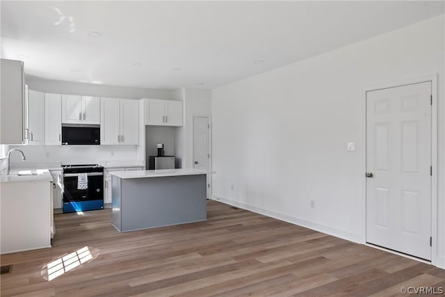 kitchen featuring electric range, light wood-style flooring, stainless steel microwave, a center island, and white cabinetry