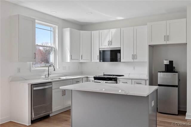 kitchen with light hardwood / wood-style floors, a kitchen island, white cabinetry, appliances with stainless steel finishes, and sink