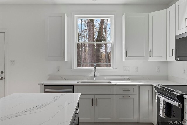 kitchen featuring appliances with stainless steel finishes, sink, light stone countertops, and a wealth of natural light