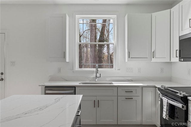 kitchen with light stone counters, appliances with stainless steel finishes, white cabinetry, and a sink